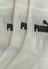 Drei Paare weißer Puma-Socken, nebeneinander gefaltet, mit gerippten Oberteilen und schwarzem Puma-Logo.
