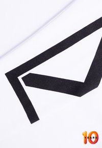 Un tessuto bianco presenta un prominente design geometrico nero, angolare e audace. Include un testo "10 ANNI" in colori sfumati nell'angolo in basso.
