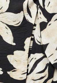 Tessuto in bianco e nero con stampa floreale che presenta grandi foglie e forme astratte, superficie testurizzata e una palette di colori neutri.