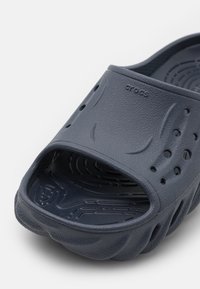 Mörkning blå slide-sandal i ett lättviktig material med textur, utrustad med ventilationshål och en böjd, formar fotbädd för komfort.