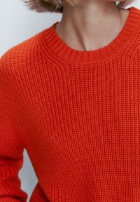 Pull en tricot épais orange avec un col côtelé et une texture. Le design comprend des manches longues et une coupe décontractée.
