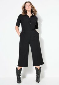 Mono corto negro de manga corta con cuello de solapa, cierre de botones, cintura elástica, piernas anchas y bolsillos laterales. Botas de vaquero negras completan el look.