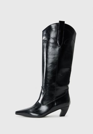 Black leather knee-high boots with a pointed toe, low heel, and decorative stitching detail on the sides. Smooth glossy finish.