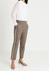 Vit långärmad topp med hög hals, i kombination med bruna byxor med rutmönster och sidostickning, samt bruna spetsiga klackskor.