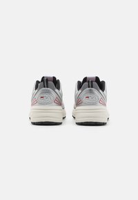 Gray athletic shoes with black accents, textured mesh upper, thick white sole, and red triangular details at the heel.