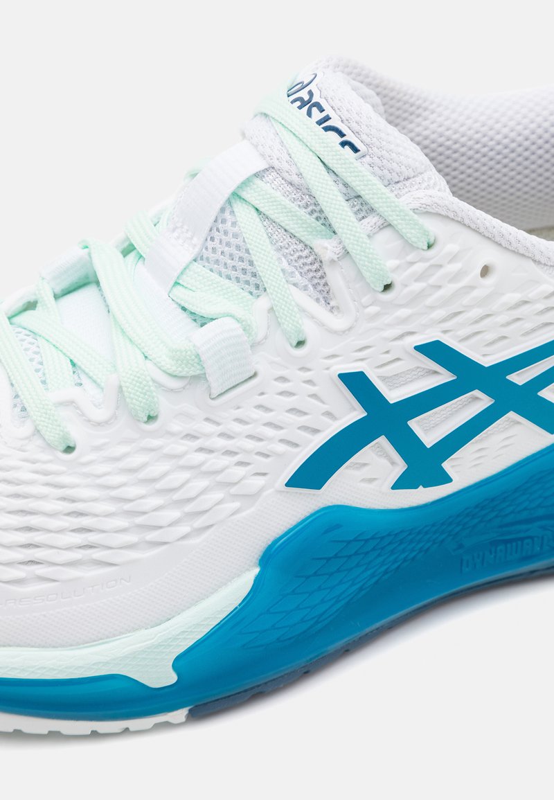 Scarpa atletica bianca con tomaia in rete, accenti turchesi chiari e una suola intermedia testurizzata. Presenta un marchio blu prominente sul lato.