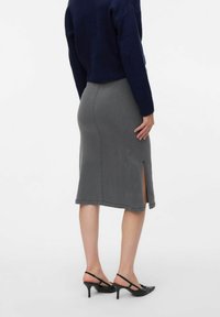 Jupe en denim gris mi-longue avec une fente sur le côté, associée à des sandales à talons noires. Le haut est un pull en tricot bleu marine.