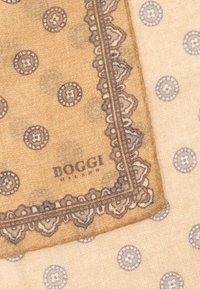 Bežový šál s tmavým vzorovým okrajom a zložitým lemovaním. V strede sú kruhové motívy rôznych veľkostí. Na ňom je tlačené meno značky "BOGGI".