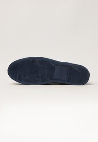 Suela de zapato azul marino con patrón de agarre texturizado, que presenta formas hexagonales y una etiqueta rectangular grabada con "42" y detalles de la marca.