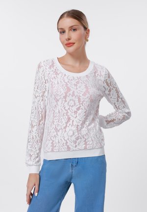 White lace sweatshirt featuring floral patterns, long sleeves, a round neckline, and ribbed cuffs and hem. Paired with light blue jeans.