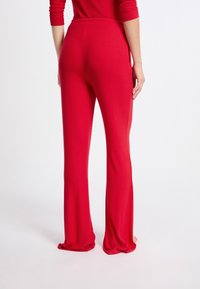 Rode uitlopende broek van zacht, rekbaar materiaal. Heeft een hoge tailleband en een gladde textuur met een vloeiende vorm van knie tot zoom.