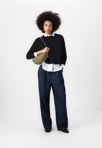 Black cropped sweater, white button-up shirt, wide-leg blue jeans, green crossbody bag, and black shoes. Curly hair styled naturally.
