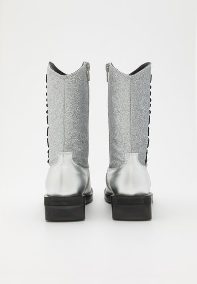Bottes de cheville en paillettes argentées avec une finition métallique lisse, fermeture éclair à l'arrière et détails en dentelle noire sur les côtés. Talon plat et épais.