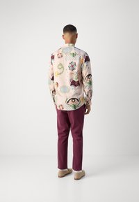 Long-sleeve shirt with a light pink base featuring colorful floral and geometric patterns. Paired with burgundy pants and beige shoes.