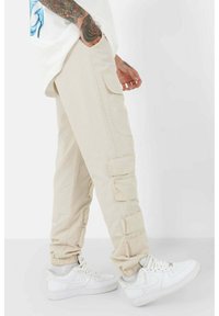 Beiga cargo-byxor med flera fickor med klaff och elastiska muddar, tillsammans med vita sneakers i låg modell. Slät bomullstyg, avslappnad passform.