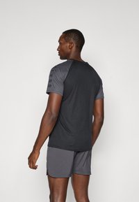 Tenue de sport pour hommes comprenant un t-shirt noir à manches courtes avec des accents gris et un détail de logo, associé à un short gris, présenté vu de dos.