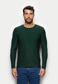 Ciemnozielona koszulka z długim rękawem, okrągłym dekoltem i dopasowanym krojem. Wykonana z gładkiego materiału, z minimalnymi szwami i bez widocznych wzorów.