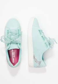Sneakers in suede verde menta con lacci in nastro trasparente, suole in gomma bianca e un accento di glitter argento di lato. Plantari rosa visibili.