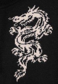 Tessuto lavorato a maglia nero con un design di drago bianco, che mette in risalto motivi testurizzati e dettagli intricati su squame e artigli.