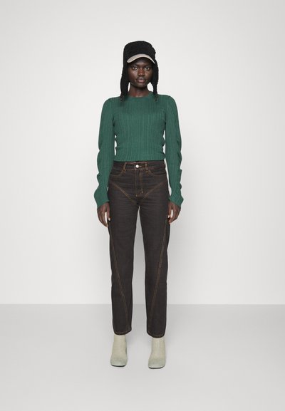 Σκούρο καφέ τζιν με εκτεθειμένες ραφές, συνδυασμένα με ένα πράσινο ριμπ μπλουζάκι και γκρί-πράσινα μποτάκια μέχρι τον αστράγαλο. Καπέλο με αυτιά.