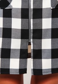 Černobílá kostičkovaná sukně s předním zipem, vyrobená z pevných tkanin a s plochými švy. Žádné viditelné kovové prvky nebo akcenty.