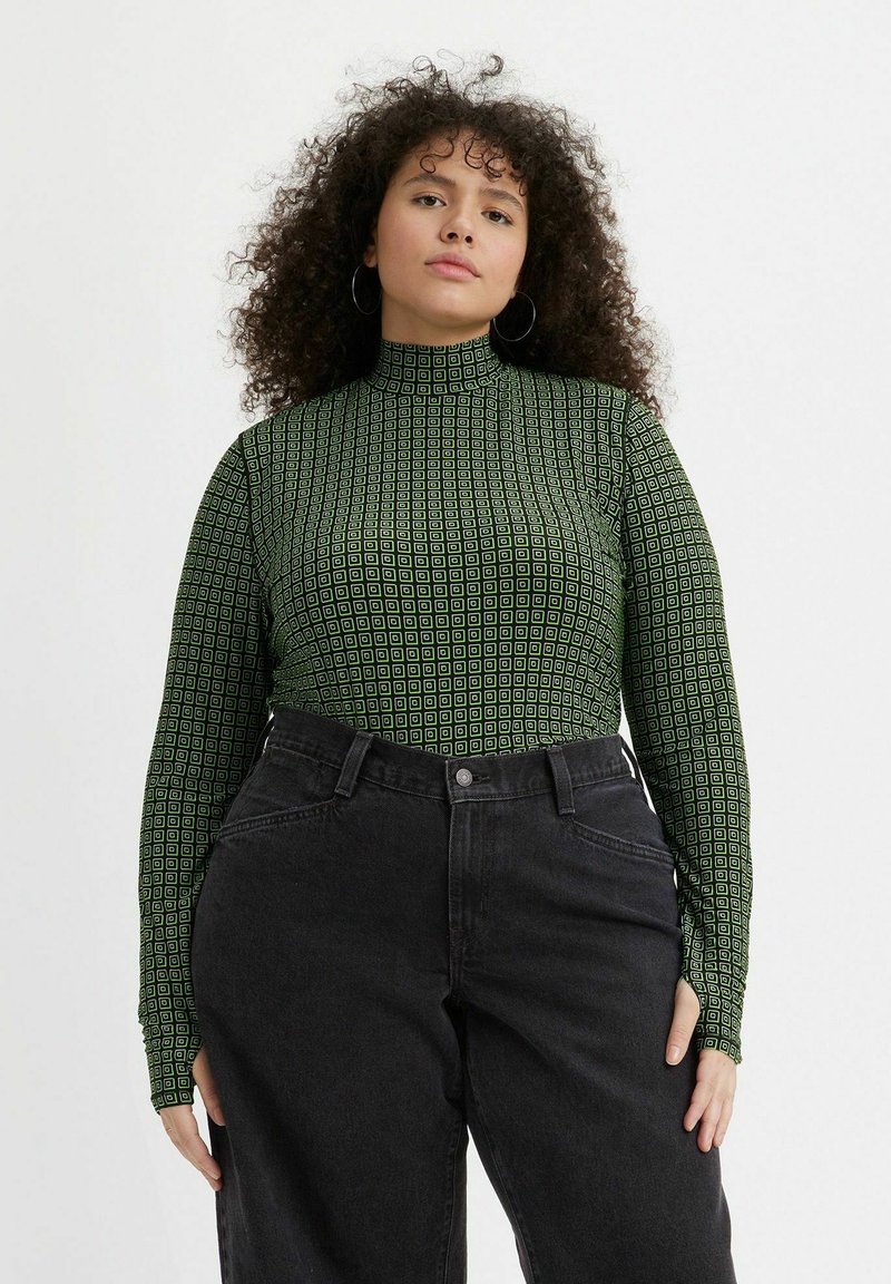 Grøn mønstret langærmet top med høj hals, med små geometriske former; parret med sorte high waist jeans.