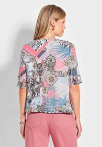 Kurzärmlige Bluse mit einem mehrfarbigen abstrakten Muster, das Farbtöne von Rosa, Blau und Tiermustern auf einem leichten Stoff zeigt.