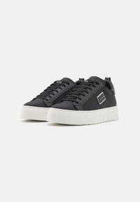 Adidași negri cu un exterior din plasă texturată, talpă din cauciuc alb, șireturi plate și un accent subtil cu un logo pătrat pe lateral.
