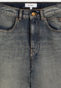 Vaqueros de mezclilla azul oscuro con un acabado desvaído, diseño de cinco bolsillos, costuras visibles y un cierre de botón de latón en la cintura. Etiqueta de marca: Scalpers.