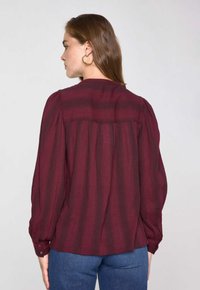 Blouse bordeaux à manches longues avec des rayures verticales, tissu texturé, poignets à boutons et un dos froncé.