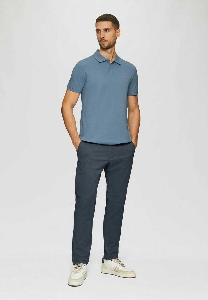 Männliches blaues Polohemd mit kurzen Ärmeln, kombiniert mit dunklen Hosen und weißen Turnschuhen. Lässiger Schnitt, glatte Textur, einfaches Design, ohne Muster.