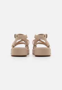 Sandali platform beige con cinturini incrociati, realizzati in materiale morbido. Punta quadrata e chiusura con fibbia regolabile sul retro. Suola piatta e testurizzata.