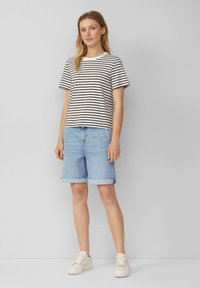 Gestreifes, kurzärmeliges T-Shirt in Weiß und Schwarz, kombiniert mit hellblauen Jeansshorts mit umgeschlagenen Säumen und weißen Sneakers.