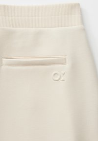 Cream-colored fabric with a ribbed waistband, welt pocket, and embossed "OX" logo near the pocket on a garment.