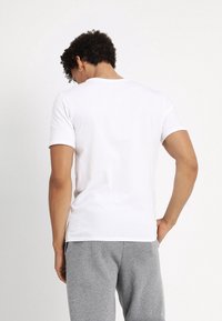 Weißes Baumwoll-T-Shirt mit kurzen Ärmeln, rundem Halsausschnitt und tailliertem Schnitt, kombiniert mit grauen Jogginghosen. Glatte Textur, einfacher Stil.