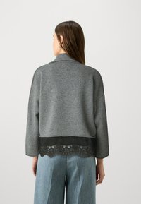 Sivkasta pleteno pulover s šalom, ki vsebuje čipkast rob na dnu čez enotno črno plast, v kombinaciji s širokimi modrimi denim hlačami.
