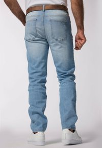 Jeans de denim azul claro con corte recto, cinco bolsillos, un ligero desgaste y un cinturón de cuero marrón, combinados con zapatillas blancas.