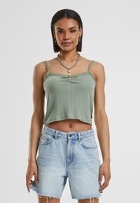 Lichtgroen geribbeld cropped tanktop met kantafwerking en een klein knoopdetail, gecombineerd met lichtblauwe versleten denimshorts.