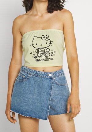 Kvinde iført en bleg gul Hello Kitty tube top og asymmetrisk blå denim nederdel med frynset kant.
