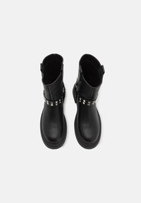 Bottines noires en cuir avec une texture lisse, bout rond et semelle plate. Comprend une sangle cloutée à mi-hauteur. Anses de tirage incluses.