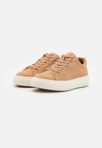 Sneakers in suede beige chiaro con lacci piatti, punta tonda e suola in gomma texturizzata. Presentano occhielli in metallo e un branding discreto sul lato.