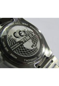 Le dos de la montre en acier inoxydable Timex présente un design de globe, avec un texte détaillant la marque et le modèle, le tout avec une finition en métal brossé et des bords lisses.