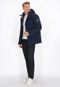 Marineblaues, isoliertes Jacket mit Reißverschluss, Kapuze und grauem Futter. Mit Druckknöpfen, seitlichen Taschen und gesticktem Logo am Ärmel.
