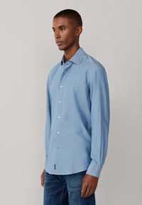 Camicia azzurro chiaro con bottoni, maniche lunghe, realizzata in tessuto liscio. Presenta un colletto standard e un orlo curvo.