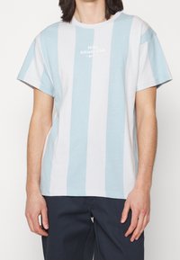 Bavlněné tričko s modro-bílými vertikálními pruhy, kulatým výstřihem a krátkými rukávy, s logem "Nike Athletic Club" v bílé barvě.