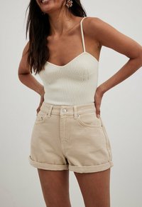 Top de tirantes de canalé crema con correas ajustables, combinado con shorts de denim beige con puños enrollados, destacando un diseño casual y ajustado.