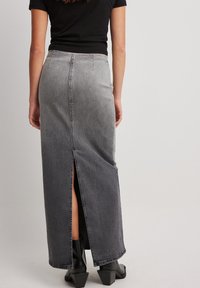 Falda maxi de mezclilla gris con una abertura trasera, que presenta un corte recto y costuras visibles. Combinada con botas negras hasta el tobillo.