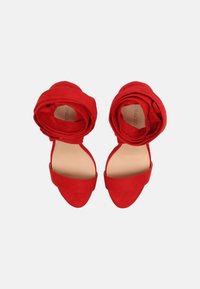 Sandales à talons hauts en daim rouge avec une large sangle sur le devant du pied et un design de bracelet de cheville enroulé. Forme à bout pointu et texture lisse.