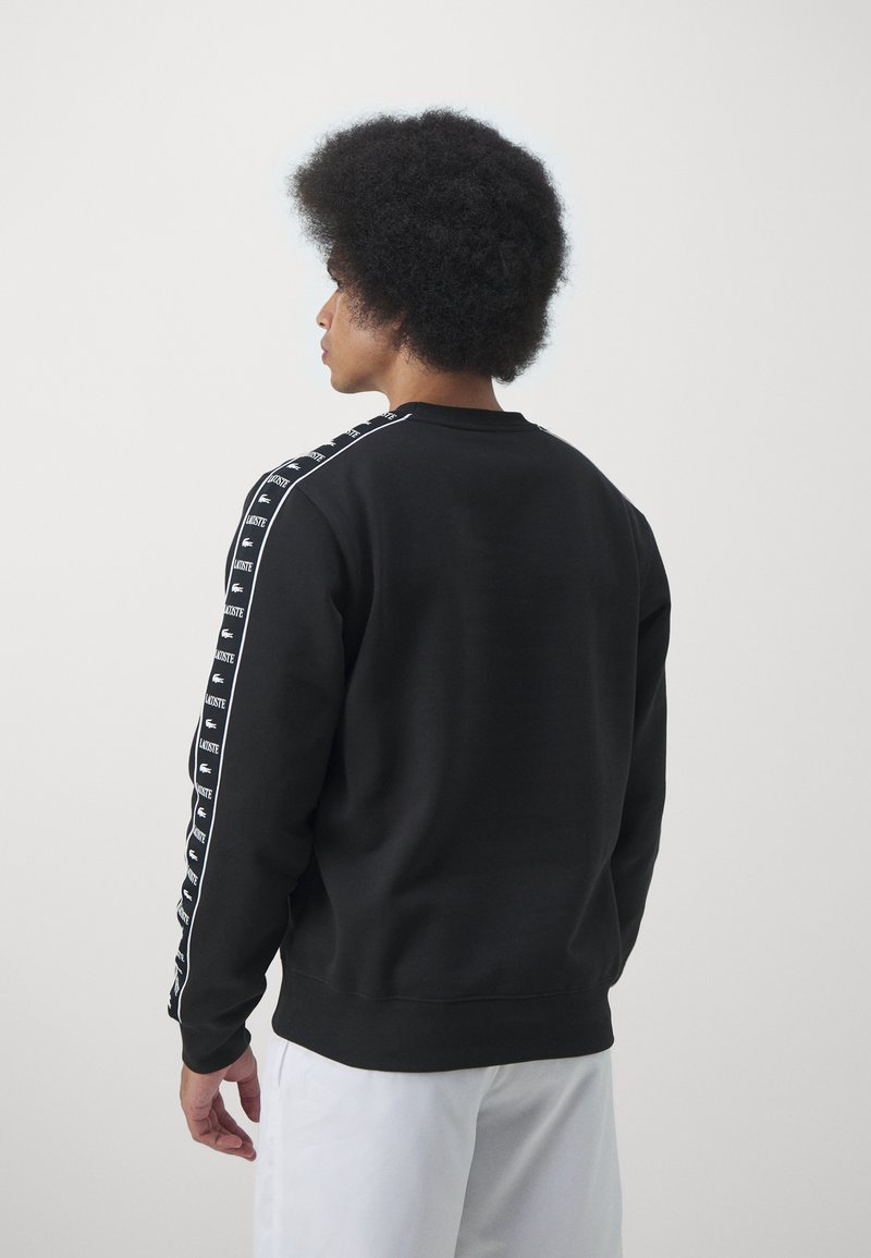 Schwarzer Sweatshirt mit Rundhalsausschnitt, kontrastierenden weißen seitlichen Streifen mit wiederholten Logos und gerippten Bündchen. Glatte Stoffstruktur.