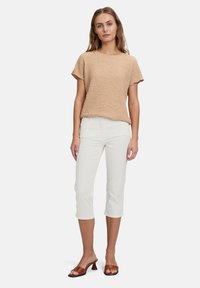 Haut en tricot texturé beige à manches courtes, associé à un pantalon court blanc et des sandales à talons marron. Design simple et décontracté.